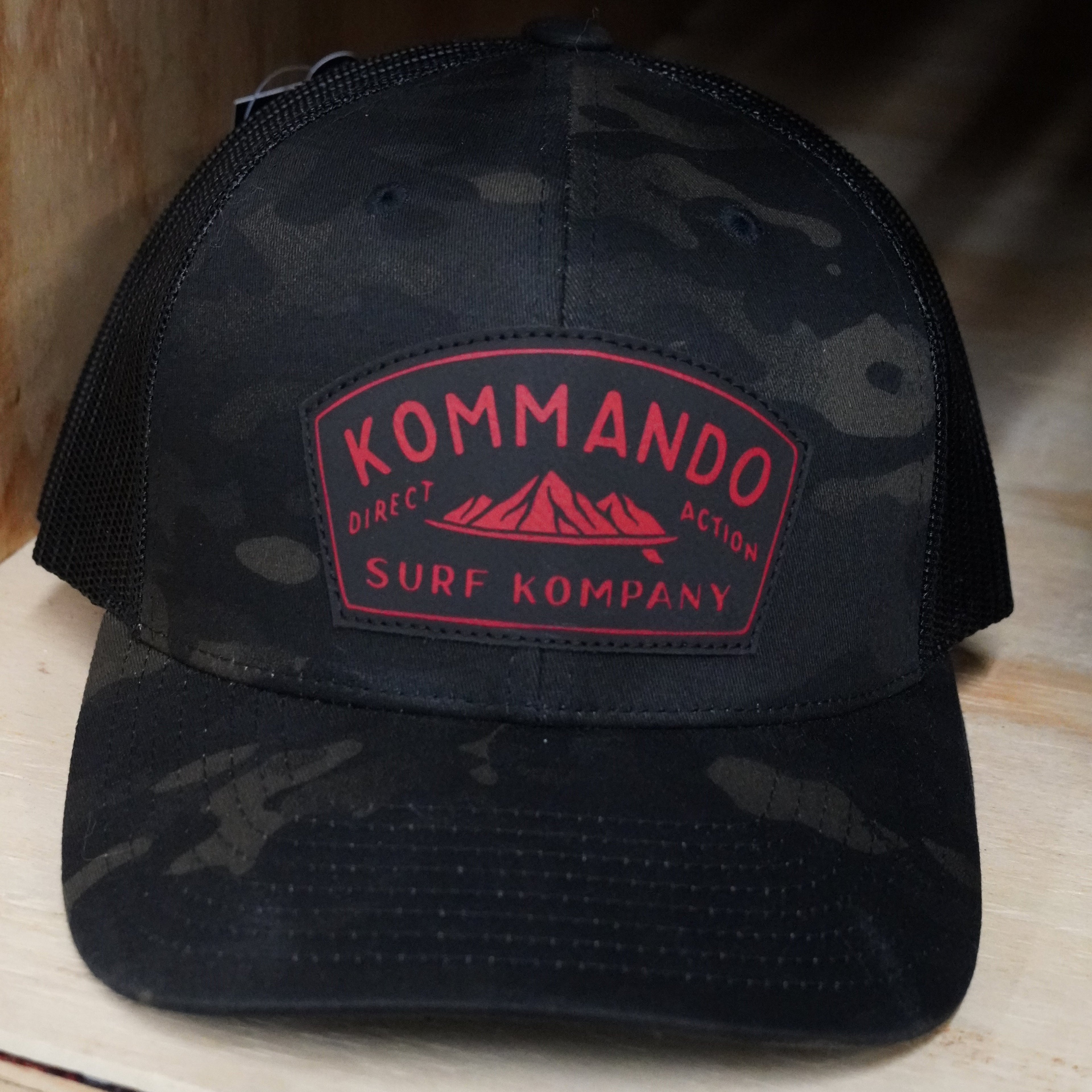 Black camouflage cap with red logo on a wooden surface